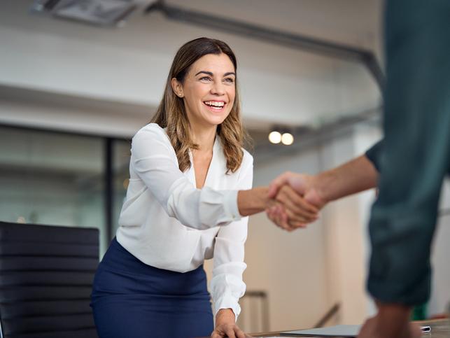 A woman shakes hand with a unseen person in an office setting